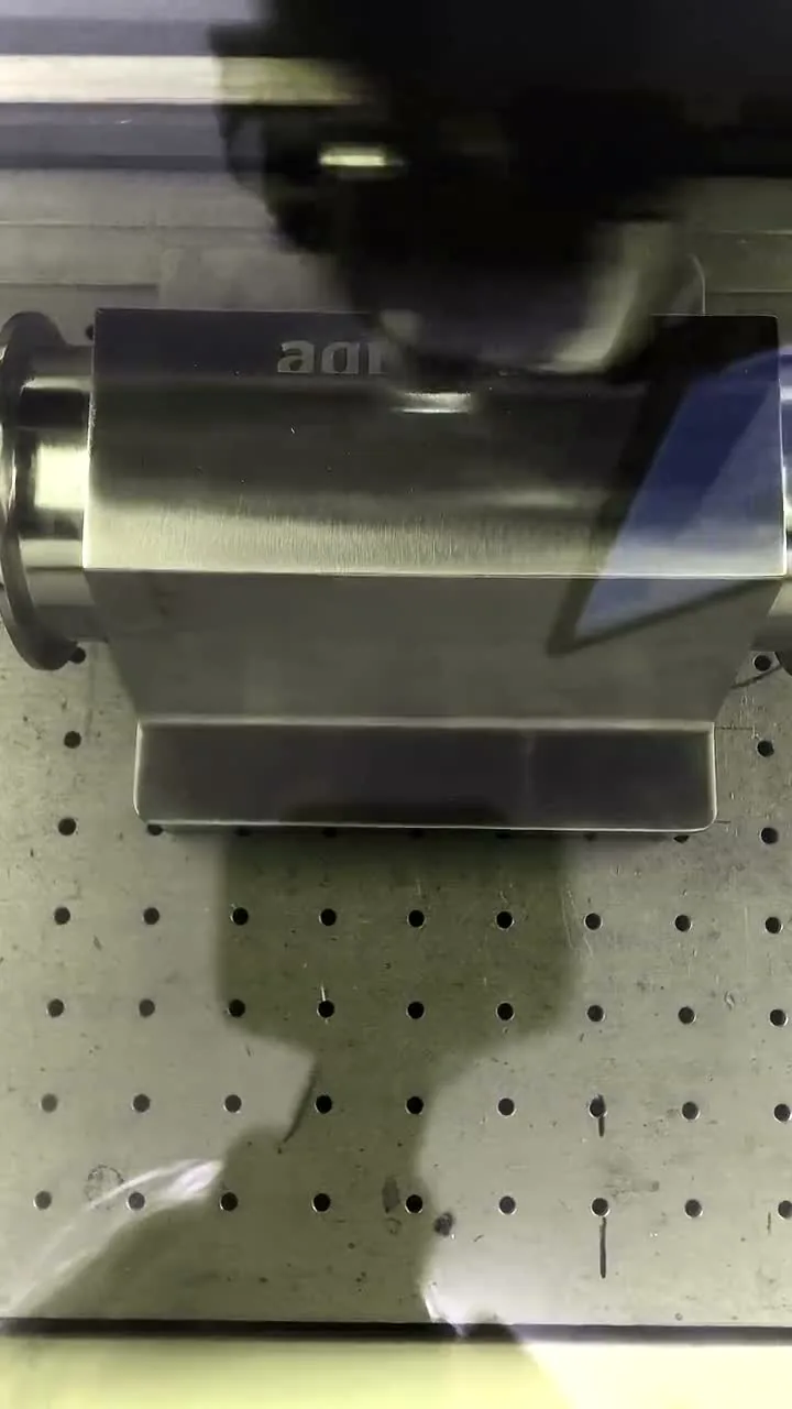 A stainless valve body being laser engraved, seen through the marker’s safety window